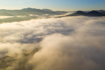 Aerial view of beautiful mountains covered with fluffy clouds on sunny day. Drone photography