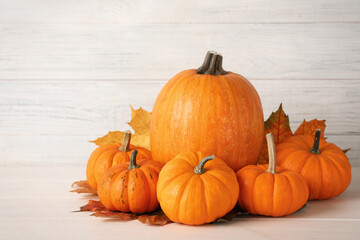 Pile of ripe pumpkins and dry leaves on white wooden table
