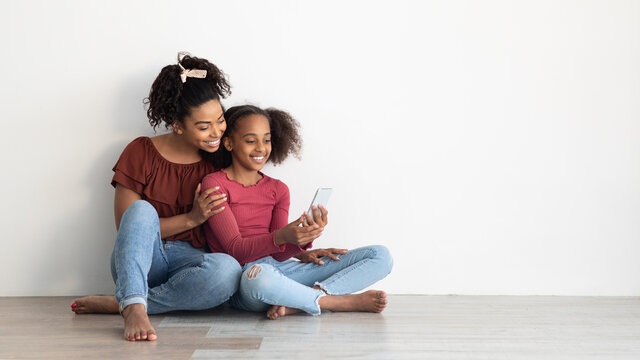 Beautiful black mother and daughter using mobile phone, panorama