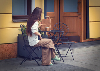 A young woman at a table in a summer caf&eacute;. A glass of coffee, a paper bag. Photography.
