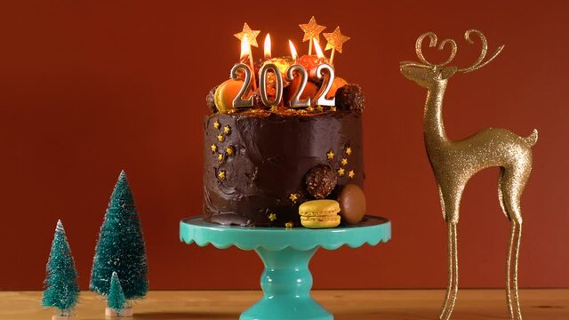 Happy New Year's Eve 2022 chocolate cake decorated with gold burning candles on aqainst dark wood table setting background. Zoom in.