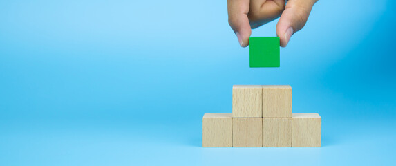 Close-up hand choose cube wooden block toy stack in pyramid without graphics for Business design...