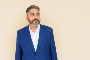 Portrait of bearded Indian businessman wearing suit against plain background