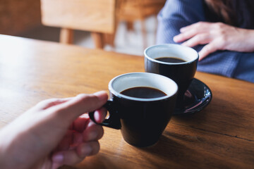 Closeup image of a man and a woman drinking and clinking coffee mugs together in cafe