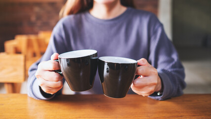 Closeup image of a woman holding and clinking two cups of coffee