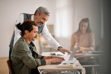 Mature teacher assists his mid adult student who is learning on laptop on computer class.