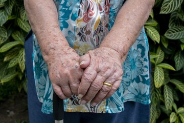Elderly hand holding a walking cane , Asian old woman standing with  hands on a walking stick