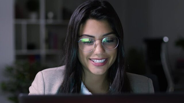 Lateral Dolly of Young Caucasian Cheerful Businesswoman in Eye Glasses Late at Night Working in Front of Computer. Office Background.