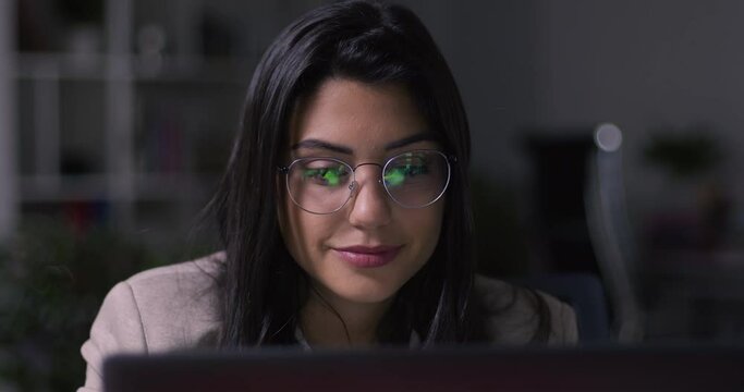 Lateral Dolly of Young Caucasian Focused Businesswoman in Eye Glasses Late at Night Working in Front of Computer. Financial Animations Reflected in Glasses. 