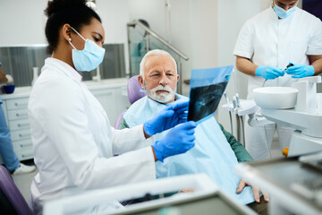 Senior man and his dentist looks at his dental X-ray during appointment at dentist's office.