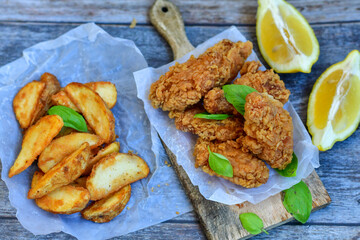  Crispy  deep fried   chicken strips ,onions and шедгес потатоес .Breaded  with cornflakes chicken  breast fillets  with chilly peppers and fresh   basil on wooden rustic background