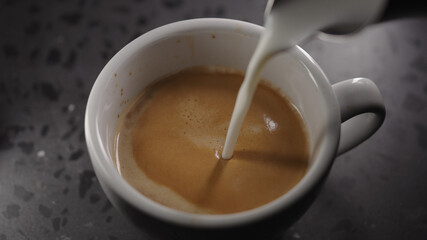 Making cappuccino, pour steamed milk into white cup with espresso