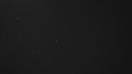 Dust particles float in neutral light on black background
