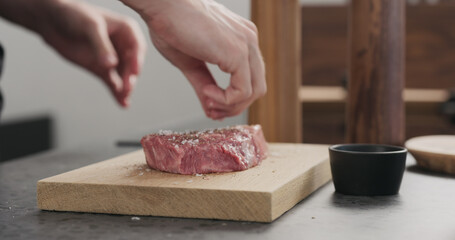 Man seasoning raw ribeye steak on oak wood board