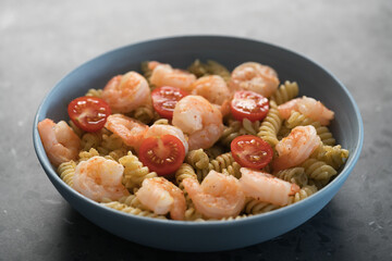 Fusilli with shrimps, cherry tomatoes and pesto in a blue bowl on concrete background