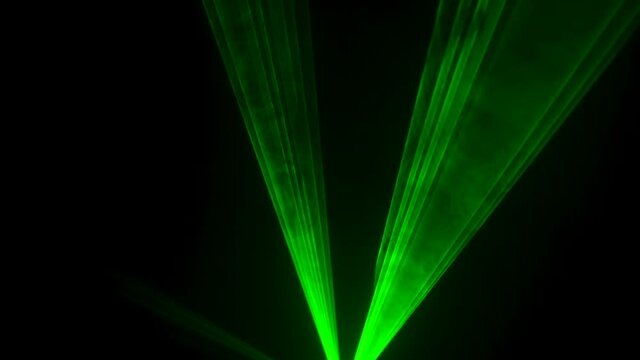 Dynamic green beams of laser neon light on black studio background spinning and strobe in puffs of smoke. Show of stage holograms. Lighting equipment and effects for holidays and parties. Close up.