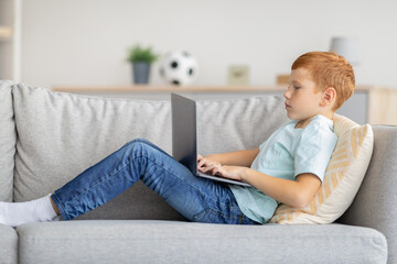 Redhead boy using laptop, playing online video game, side view