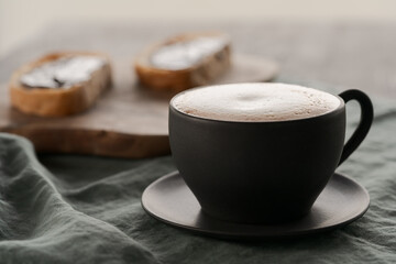 Cappuccino in black cup with ciabatta slices with chocolate spread on background