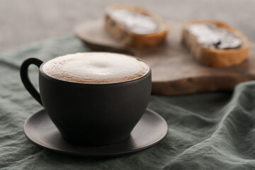 Cappuccino in black cup with ciabatta slices with chocolate spread on background