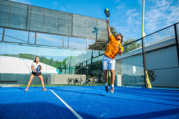 Mixed padel match in a blue grass padel court - .Beautiful girl and handsome man playing padel...