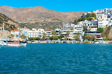 Fototapeta na wymiar View across the harbor to the promenade and the fishing boats of the popular resort of Agia Galini on the south coast of Crete. The village was already settled in the times of the Minoan culture