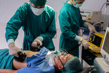 Doctor and nurse using defibrillator to pump at chest of unconscious with low heart rate patient to save life while doing medical surgery inside of operating room. Emergency aid, CPR.