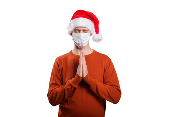 Fototapeta na wymiar an isolated shot of a believing man in a medical mask, in casual clothes, a Christmas hat. He folded the palms of his hands together at his chest, prayed, asked God, closed his eyes
