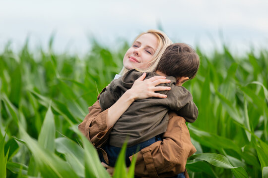 Blonde mother in cloak with a child boy in cornfield in summertime