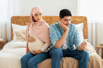 Young pregnant muslim woman offended to her husband busy with smartphone, arab lady in hijab feeling lonely