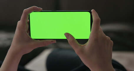 Young woman lying on a couch and using smartphone with horizontal green screen