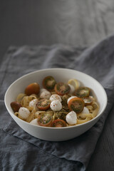 Fettuccine with mozzarella, tomatoes and pesto in white bowl on black table