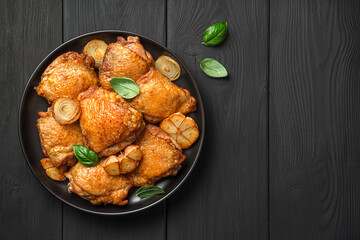 Chicken thighs with fried onions, garlic and fresh basil on a black background. Top view, copy space.