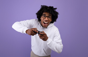 Excited black teenager with joystick playing video game on violet studio background © Prostock-studio