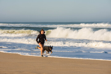 beautiful young athletic woman running with her dog on the beach
