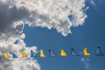 Yellow and blue triangular festival flags on sky background with white clouds. Outdoor Celebration Party