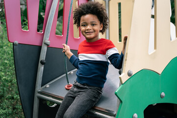 Happy kid boy with afro hair in playground in the park