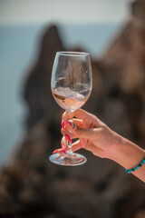 A female hand holds a glass of wine against the background of the sea and mountains.