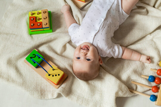cute newborn baby in light clothes is playing with educational toys lying on the floor on a gray linen blanket. top view. products for children. happy childhood and motherhood. space for text