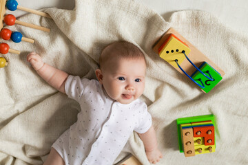 cute newborn baby in light clothes is playing with educational toys lying on the floor on a gray...