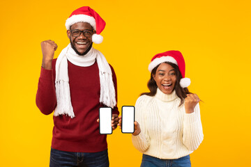 Black Couple Showing Smartphones Gesturing Yes Wearing Santa Hats, Studio