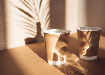 Creative composition made of two paper cups on sunlit background with shadows. Minimal style. Morning drinks concept.