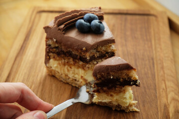 Piece of Kiev cake with chocolate icing and blueberries on wooden board. A bite of cake on a fork