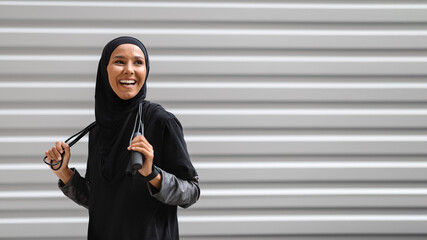 Cheerful Young Muslim Woman In Modest Sportswear Posing With Skipping Rope Outdoors