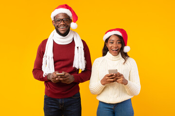 Fototapeta premium African American Couple Holding Smartphones Wearing Santa Hats, Studio Shot