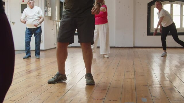 Senior people having dance class with teacher in ballroom. Close-up shot of dancers legs in sneakers moving and stepping side to side on floor. Community, hobby, retirement concept