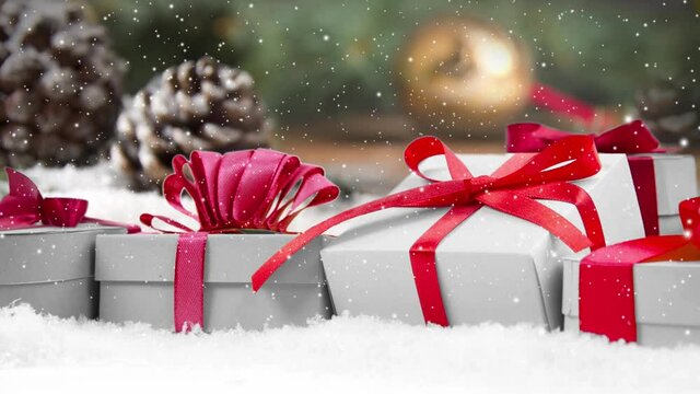 Still life with gift row on snow covered surface. Pine cones, and spruce branches in the background. Falling snow effect. Christmas, holiday and winter concept. High quality 4k video.