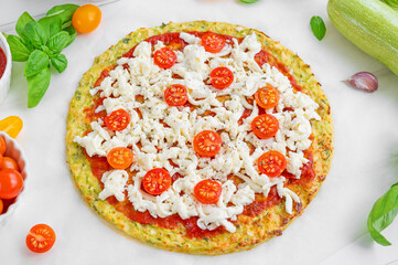 Preparation zucchini crust pizza with tomato sauce, mozzarella cheese, fresh tomatoes and basil on a white wooden background. Zucchini pizza Margarita. Healthy dish.