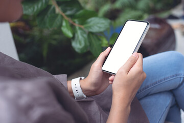 Mockup image of woman sitting cross legged using white mobile phone with blank black screen 