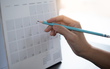 Close-up of business woman taking note on calendar desk, making agenda on office table. Event planner timetable. Calendar event plan