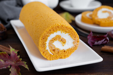 Pumpkin cake roll with cream cheese filling on a dark wooden background. Dessert for Thanksgiving or Halloween. Selective focus, copy space.